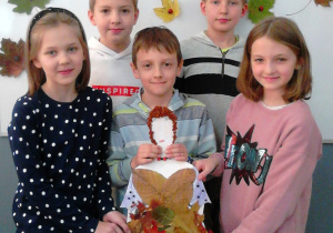 Pięcioro uczniów przytrzymuje wykonaną przez siebie postać Pani Jesieni. W tle tablica z przyczepionymi liśćmi.